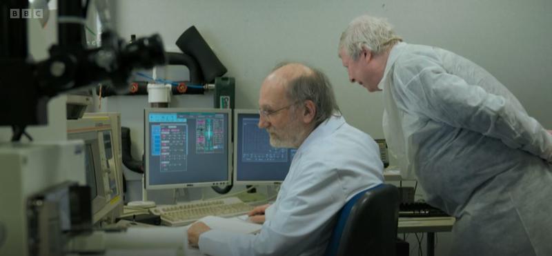 Dr Chris Salter seated at a desk with two monitors, and Prof Peter Northover standing and leaning forward, viewing the same data 