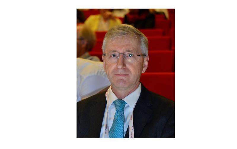 Head and shoulders of professor todd wearing a suit and tie in a room with tiered seats and golden lighting