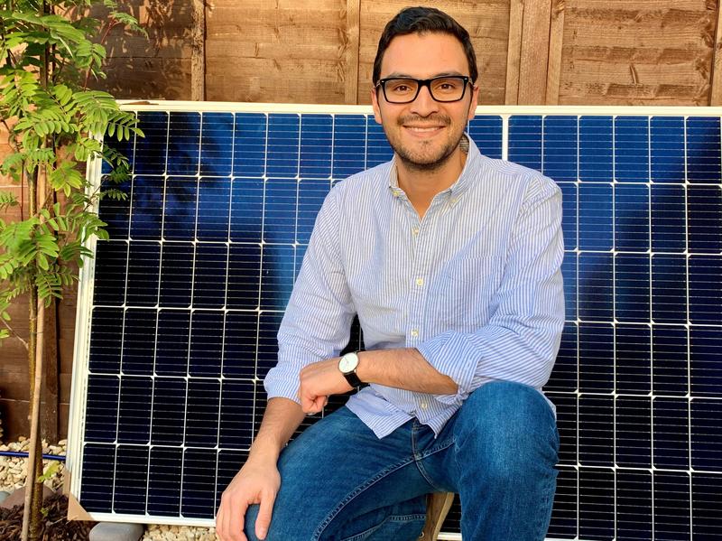 Professor Bonilla kneeling in front of a solar panel