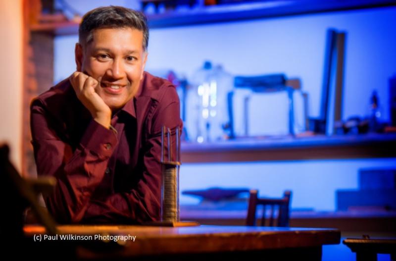 Professor Islam sitting in an illuminated lab leaning forward and smiling