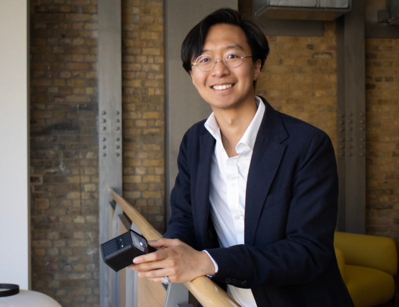 Dr Hans Chan in a suit leaning against a balustrade and holding one of his detectors